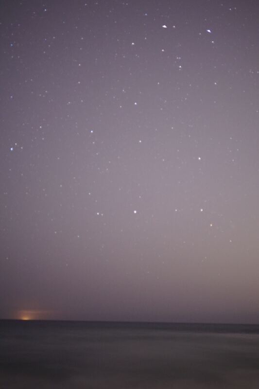 Stars scattered across a violet night sky above a dim ocean horizon, in a tall frame.